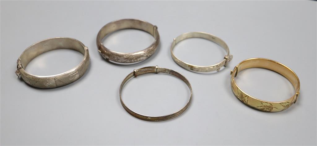 Four assorted silver bangles and a gold plated bangle.